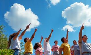 Group of people looking at interesting cloud formations in a clear sky, pointing with enthusiasm, at an outdoor event.